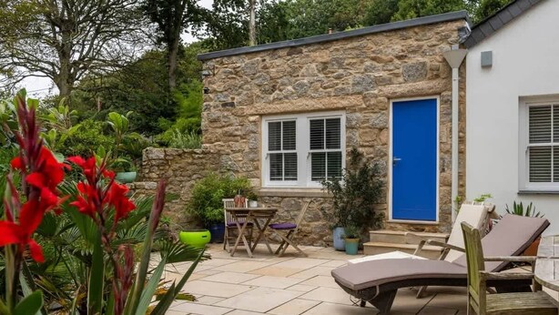 A stone building with a blue door, a small window, and a patio area with outdoor furniture. - Stunning 1 Bed~ River view~ parking~central (Newlyn)