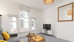 A modern living room with a grey sofa, yellow cushions, a wooden coffee table, and a TV on a white stand.