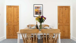 A dining area with a wooden table and chairs, a vase with flowers, and a framed picture on the wall.