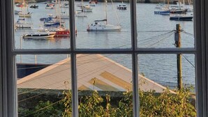 A view through a window of a marina with multiple boats docked, a hilly landscape in the background, and a clear sky. - Breathtaking views on historical street- central (Penzance)