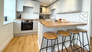 A modern kitchen with white cabinetry, a herringbone tile backsplash, a central island with stools, and a built-in oven. - Breathtaking views on historical street- central (Penzance)