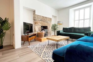 A living room with a stone fireplace, a television, a sofa, and a coffee table. - Stylish Marazion Retreat • Sleeps 6 • Garden & Fireplace” (Marazion)