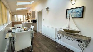 A modern kitchen with a dining area, featuring a glass table, white chairs, and a white radiator.
