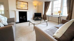 A living room with a fireplace, a television, and a glass coffee table.