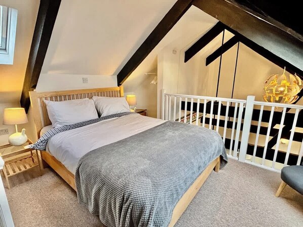 Un dormitorio con cama, mesitas de noche, lámpara y cuna.