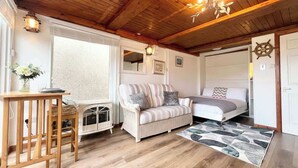 A cozy room with a wooden ceiling, a striped sofa, a bed, and a small table with a vase.