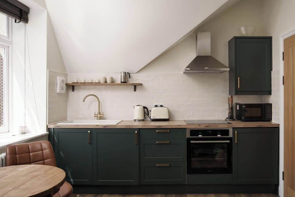 Una cucina moderna con pensili verde scuro, un piano di lavoro bianco, forno integrato e microonde.