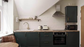 Una cucina moderna con pensili verde scuro, un piano di lavoro bianco, forno integrato e microonde.