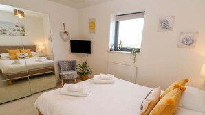 Habitación de hotel con una cama grande, un espejo, televisor, ventana y una planta en maceta.