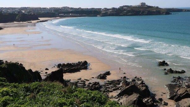 Una playa costera con afloramientos rocosos, una orilla arenosa y un edificio distante en una colina.