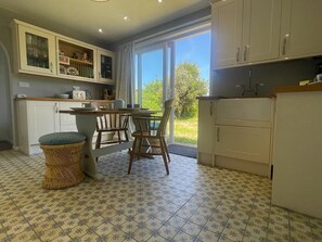 Una cocina con armarios blancos, una mesa de comedor con sillas y un ventanal grande.