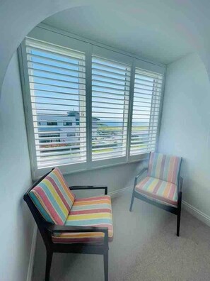 A corner room with two striped chairs and a window with blinds.
