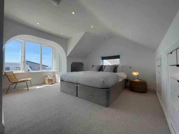 A bedroom with a large bed, a window, a chair, and a bedside table.