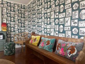 Una habitación con una pared adornada con fotografías enmarcadas, un banco de madera con cojines de colores y un reposapiés redondo pequeño.