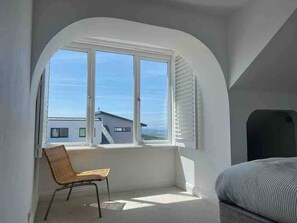 Una habitación con un amplio ventanal de arco, una silla de mimbre y una cama.