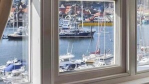 A room with a large window overlooking a marina with boats and buildings. - Waterfront Cottage by Whitby Harbour + (Whitby)