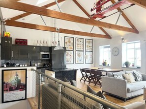 A modern kitchen with a dining area, featuring a high ceiling with exposed beams, a dining table with chairs, and a sofa. - Stylish~Tasteful~2Bed~2Bath~Central~Townhouse (Penzance)