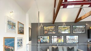 Una sala de estar con un sofá gris, piso de madera y una pared de galería con diversas obras de arte enmarcadas.