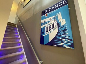 A staircase with a handrail and a wall-mounted poster advertising a hotel. - Stylish~Tasteful~2Bed~2Bath~Central~Townhouse (Penzance)