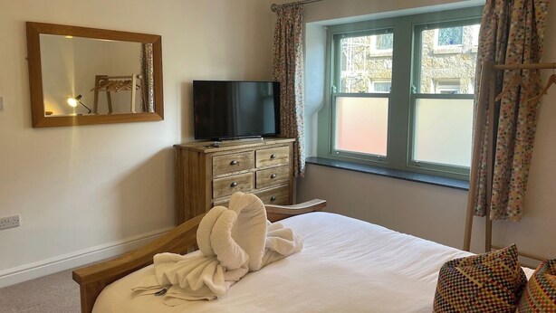 Una habitación de hotel con una cama, televisión, cómoda, ventana con cortinas y un espejo en la pared.