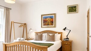 Un dormitorio con una cama de madera, una mesita de noche con lámpara, un perchero y un cuadro en la pared.