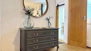 A dark wooden dresser with ornate handles, a round mirror above it, and a vase with flowers on top. - The Coach House, Penzance- Cosy Nook for 2 (Penzance)
