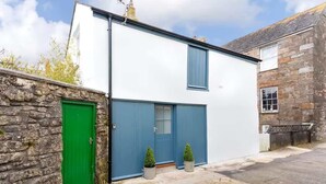 A two-story building with a white facade and blue shutters, a green door, and two potted plants at the entrance. - The Coach House, Penzance- Cosy Nook for 2 (Penzance)