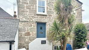 Ein Steinhäuschen mit blauer Tür, einem Schild mit der Aufschrift 'Boatman's Cottage 2 Mill Lane' und einem weißen Zaun davor.