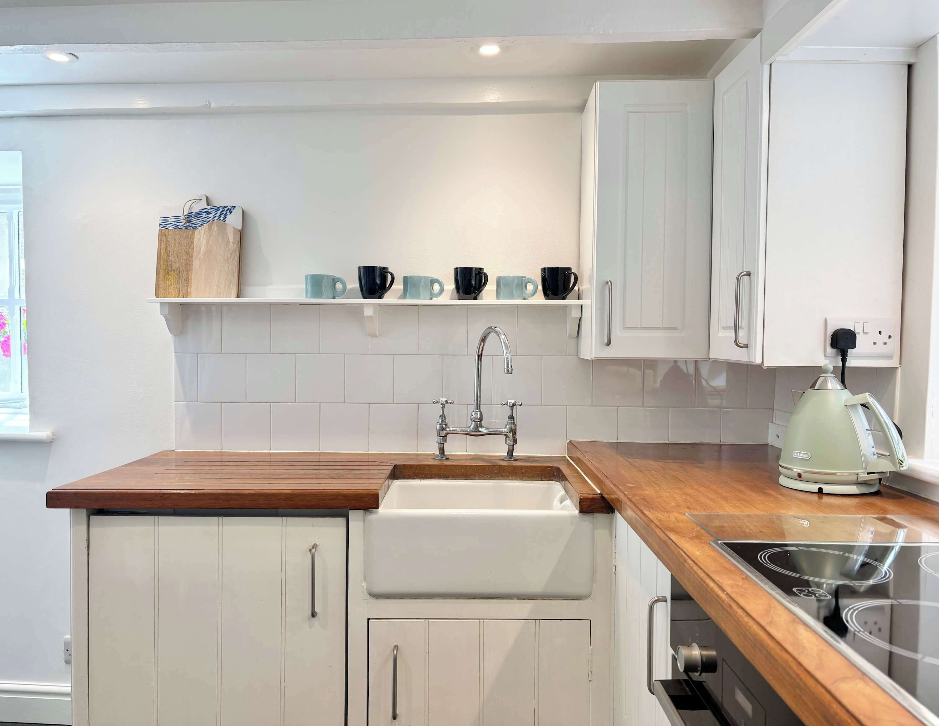 A kitchen with white cabinets, a wooden countertop, a sink, a kettle, and a coffee maker.