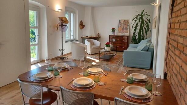 Un comedor con una mesa de madera dispuesta para seis personas, rodeada de sillas. Hay un ventanal con vistas a zonas verdes.