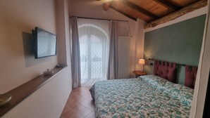 Una camera da letto con un letto, un comodino, una lampada, una finestra con tende e un soffitto in legno.
