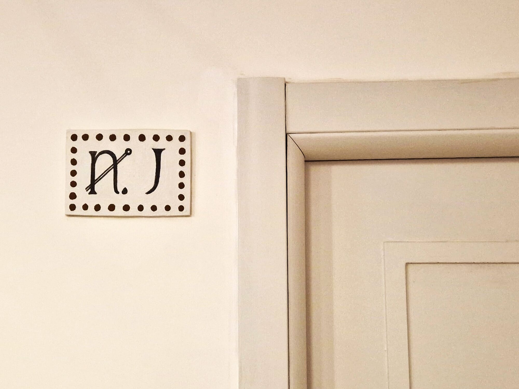 Una placa en la pared con las letras 'P.J.' y una puerta de diseño sencillo.