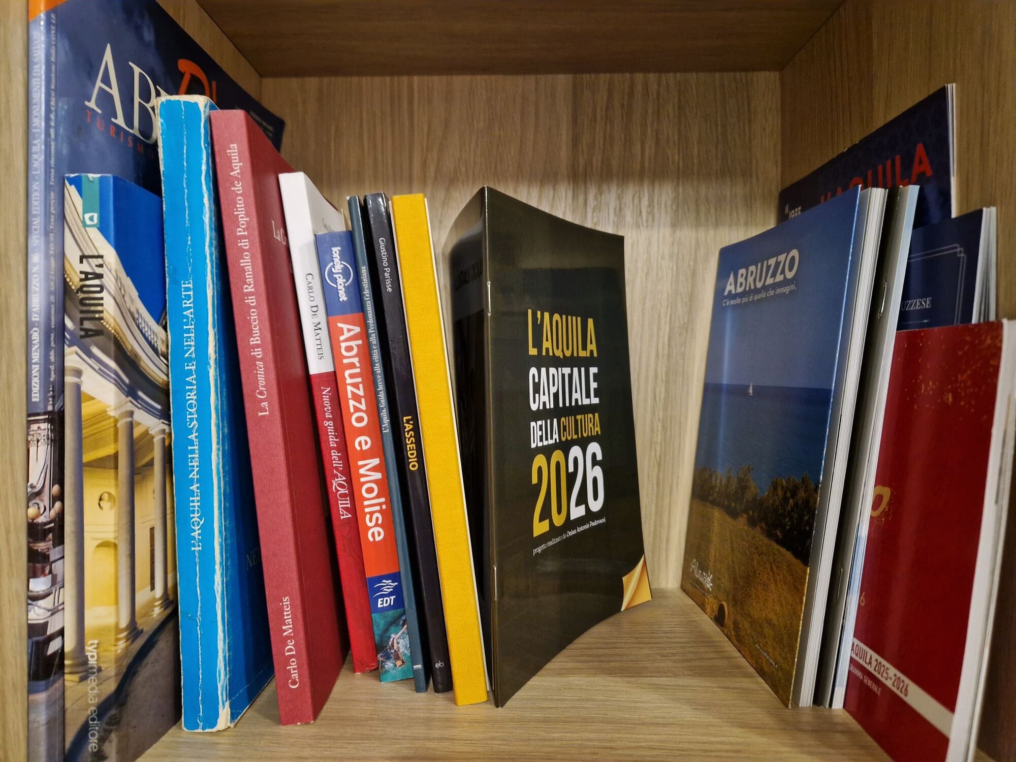 Kirjahylly, jossa on monenlaisia kirjoja, muun muassa teoksia, joiden nimissä on esimerkiksi sanat ’Abruzzo’ ja ’L’Aquila Capitale 2026’.