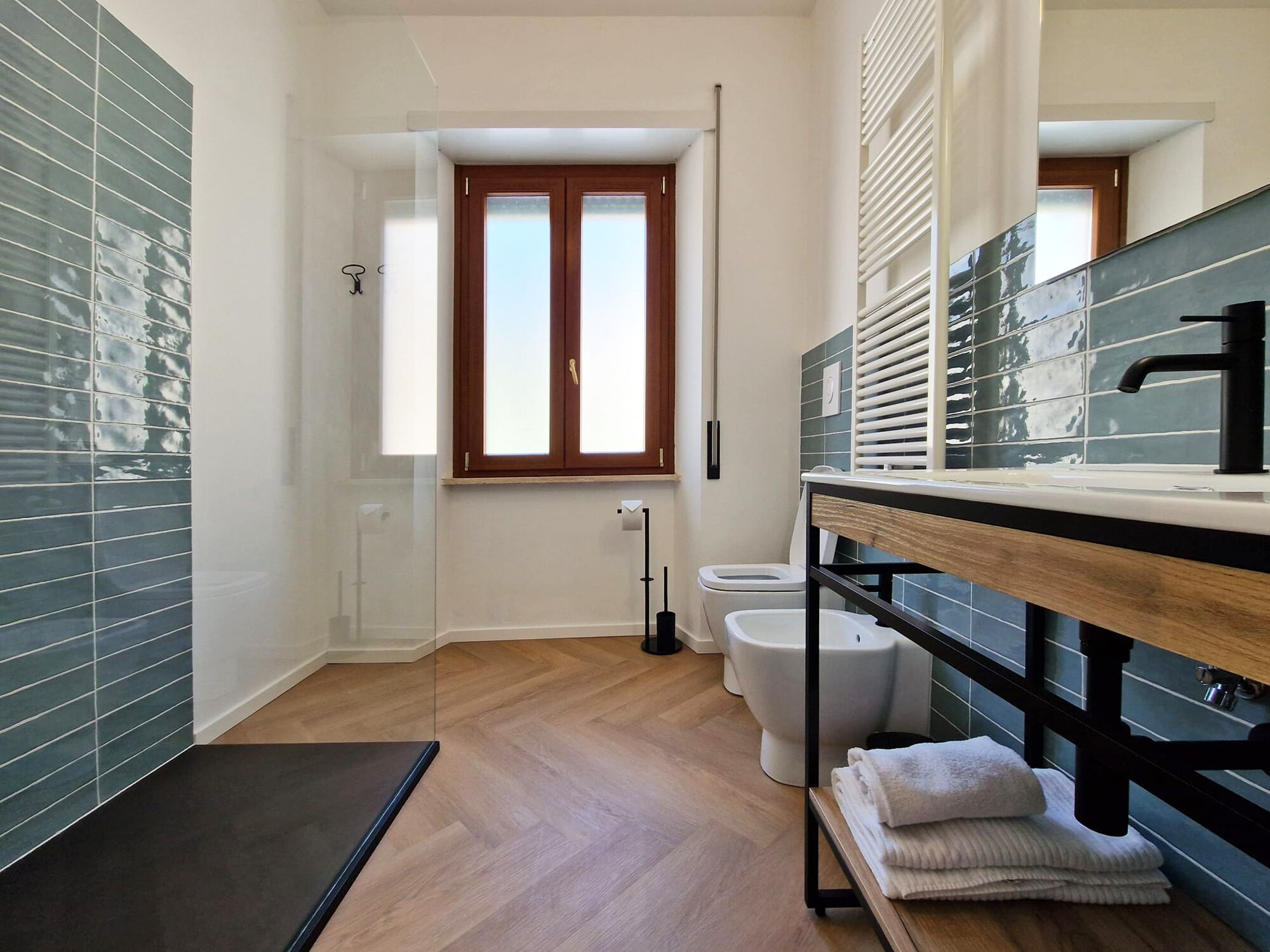 A modern bathroom with a wooden floor, a large mirror, and a window.
