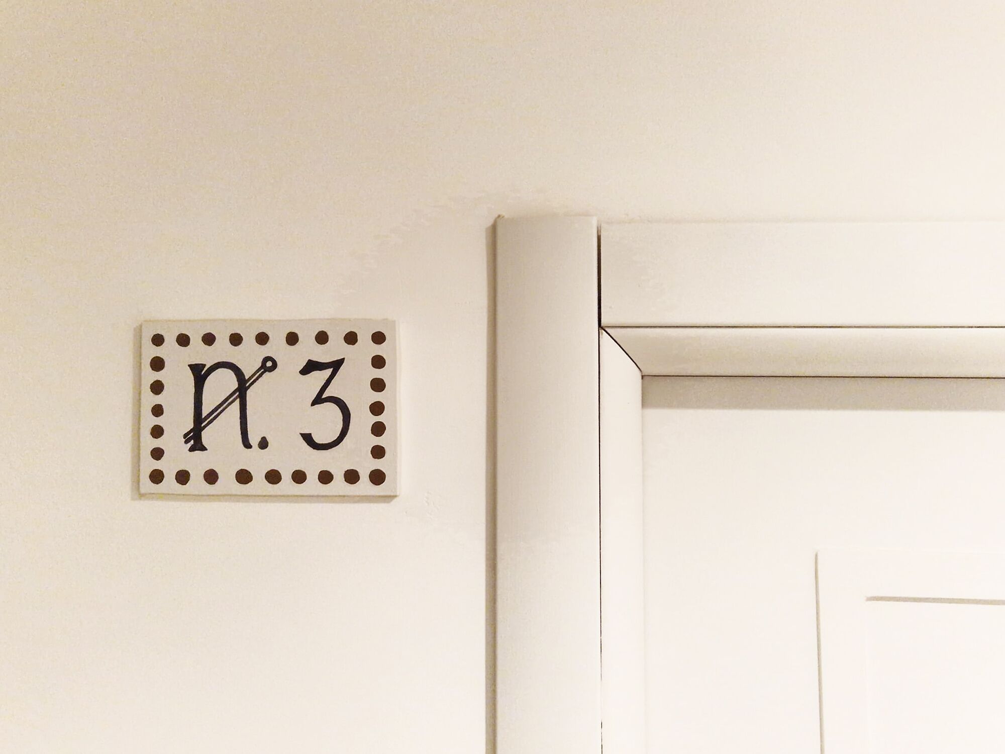 A white door with a small sign above it that reads 'n.3' with a dotted border.