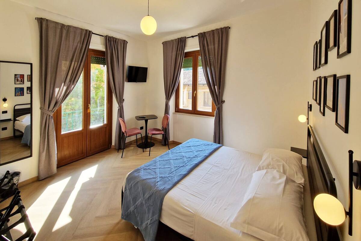 Une chambre d’hôtel avec un lit, un bureau, deux chaises, une télévision et des rideaux.