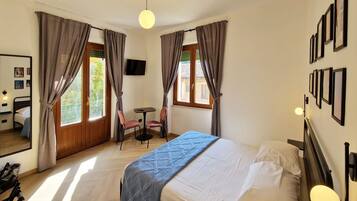 A hotel room with a bed, a desk, two chairs, a TV, and curtains.