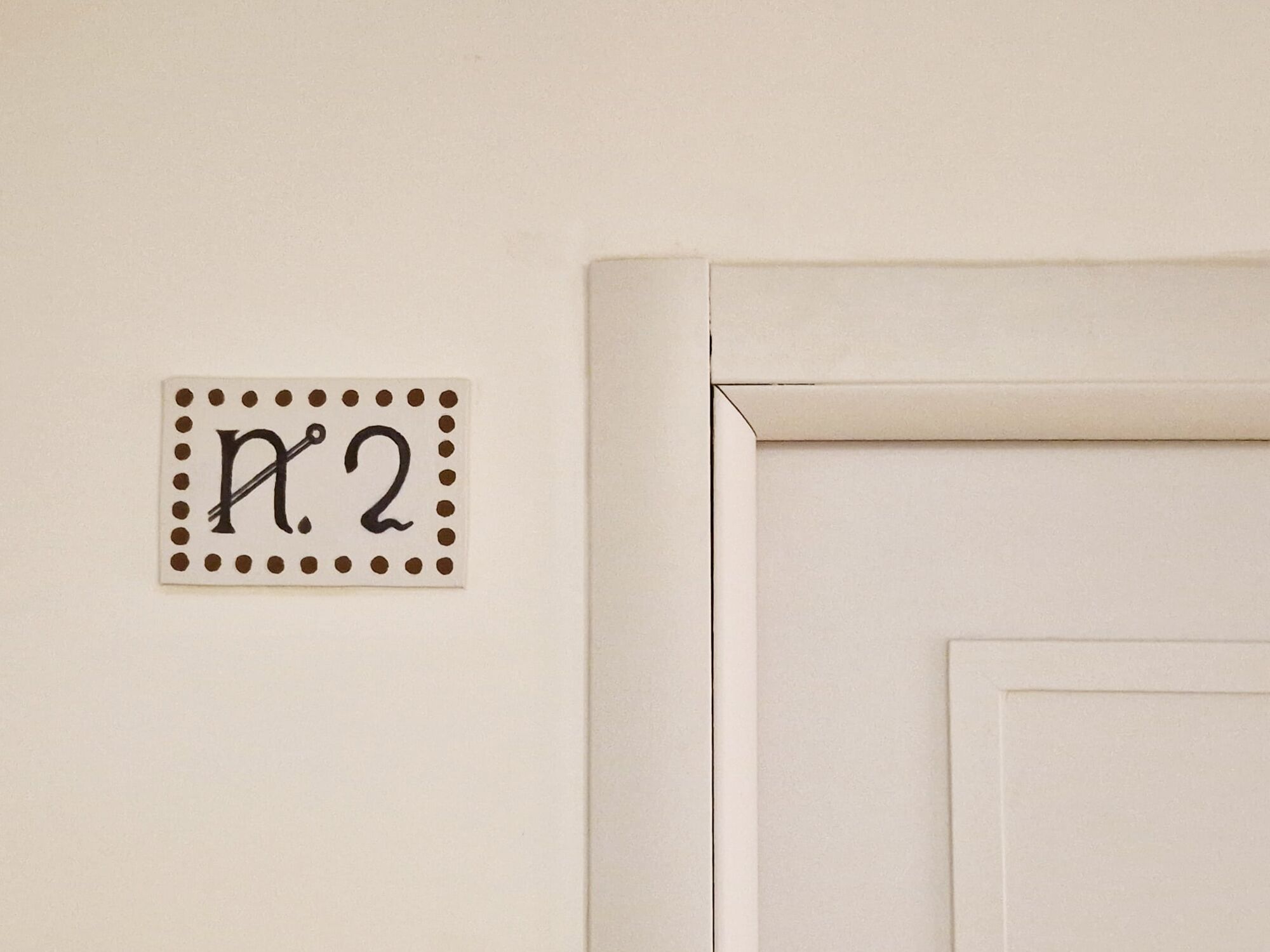 Señal en la pared con el número 2 y un borde decorativo, que indica un número de habitación.
