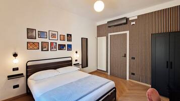 A modern bedroom with a bed, bedside tables, wall-mounted artwork, a wardrobe, and a hanging light fixture.