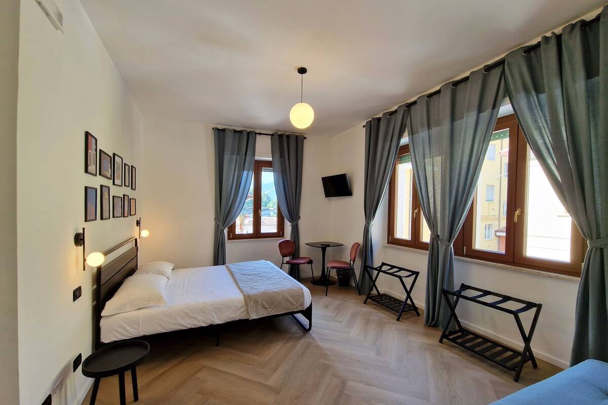 Une chambre d’hôtel avec un lit, une petite table, une chaise, un téléviseur et une fenêtre avec des rideaux.
