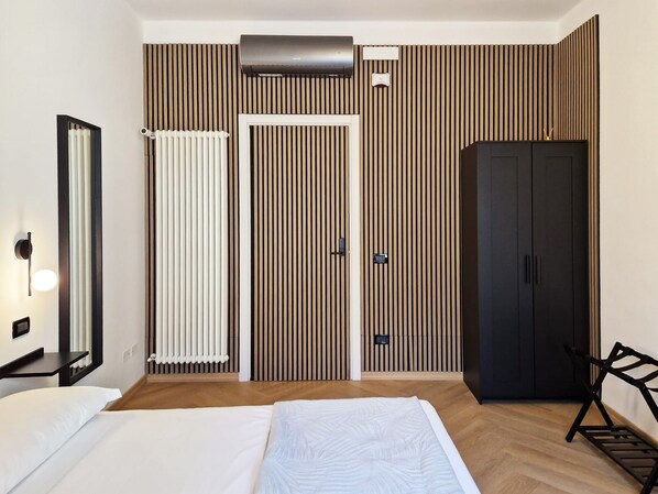 Una habitación de hotel moderna con cama, armario, radiador y aire acondicionado instalado en la pared.