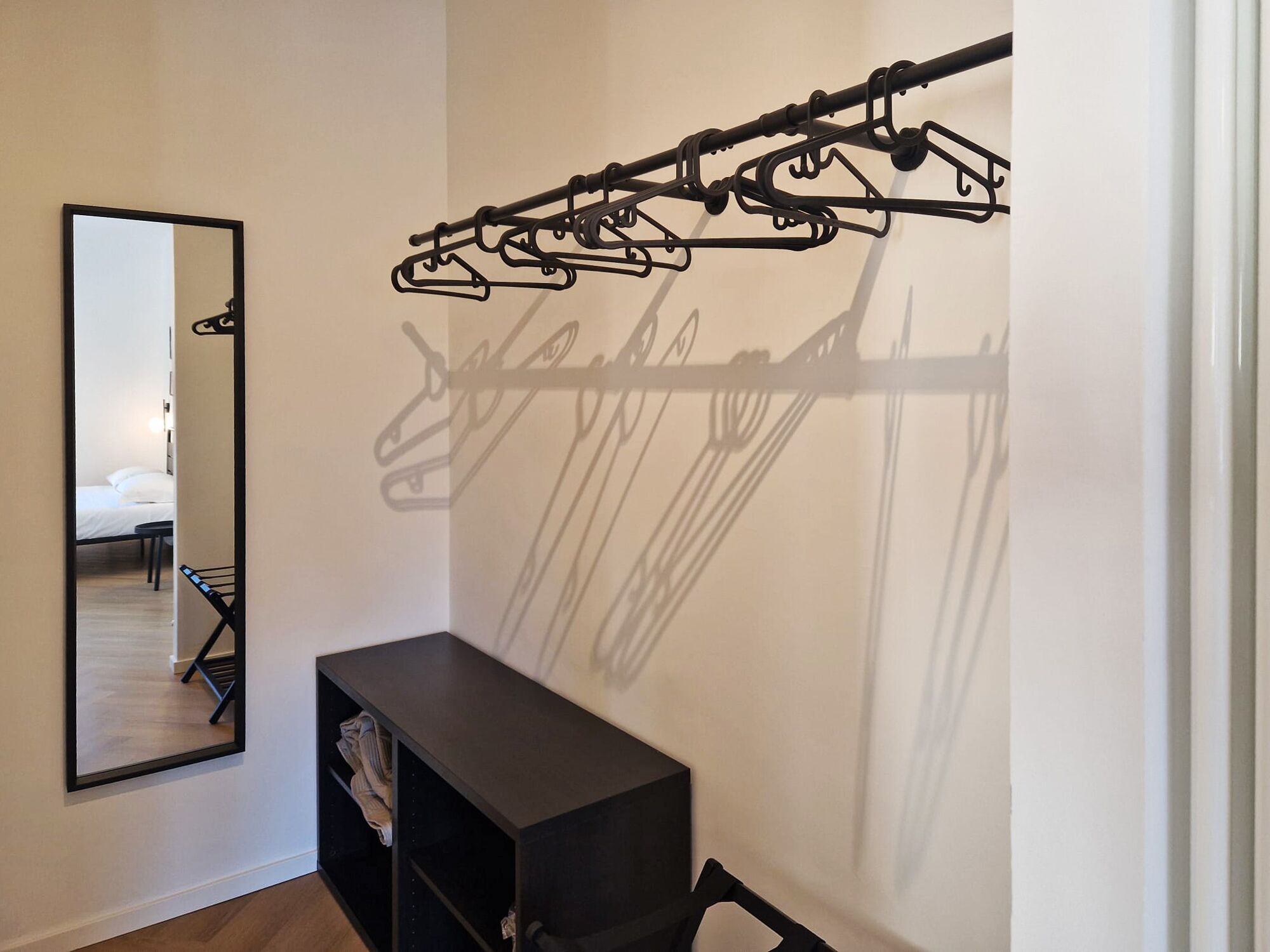 A hotel room with a large mirror, a black storage unit, and a wall-mounted coat rack.