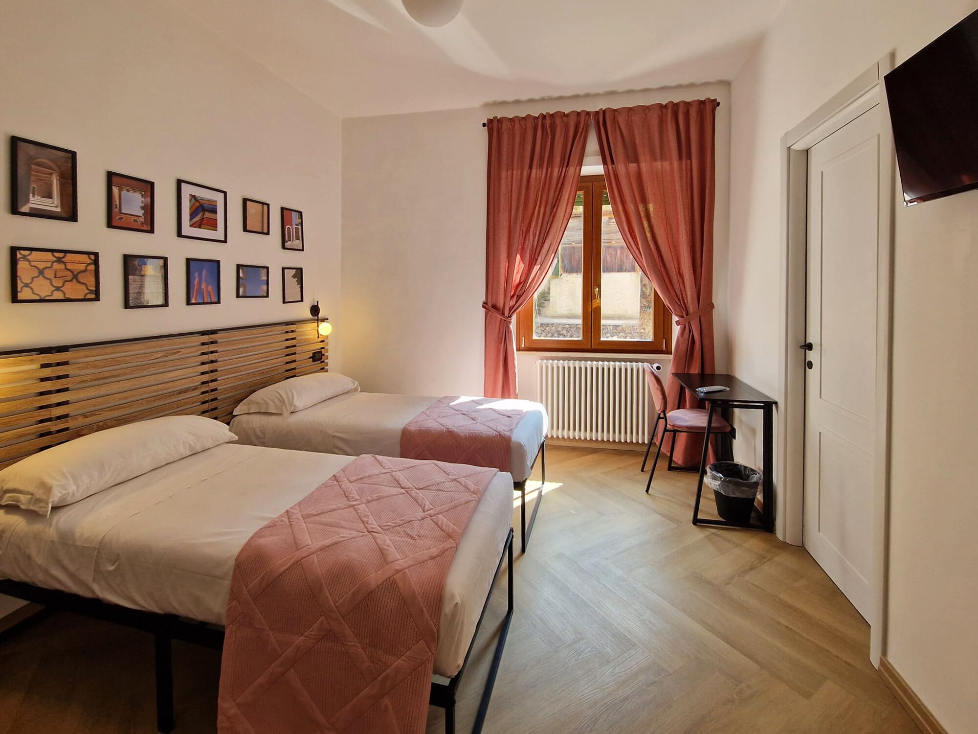 Un dormitorio con dos camas, una ventana con cortinas, un radiador, un televisor y cuadros en la pared.