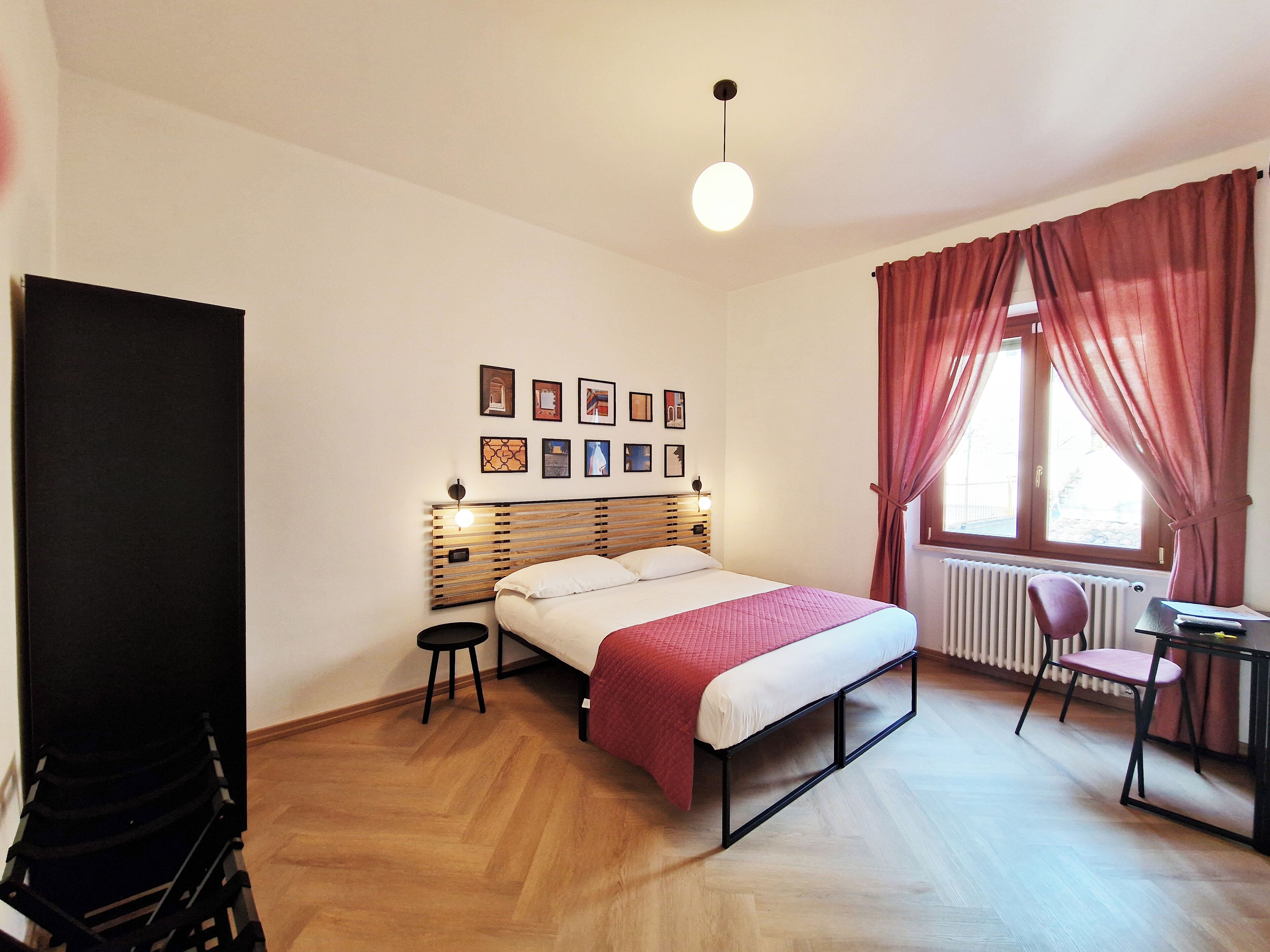 A bedroom with a bed, a desk, a chair, a radiator, and a window with curtains.