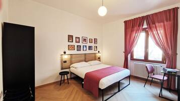 Un dormitorio con cama, escritorio, silla, radiador y ventana con cortinas.