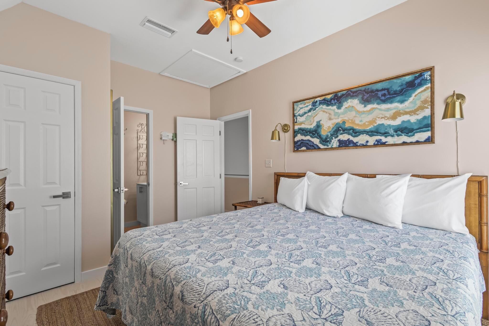 A bedroom with a bed, a ceiling fan, a painting, and a lamp.