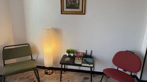Una stanza con una poltrona verde, una poltrona rossa, un lampadario ad arco, un tavolino con libri e una pianta, e un quadro appeso al muro.