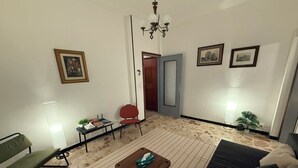 Un soggiorno con un divano, un tavolino, una poltrona rossa, una lampada e una porta che dà su un'altra stanza.