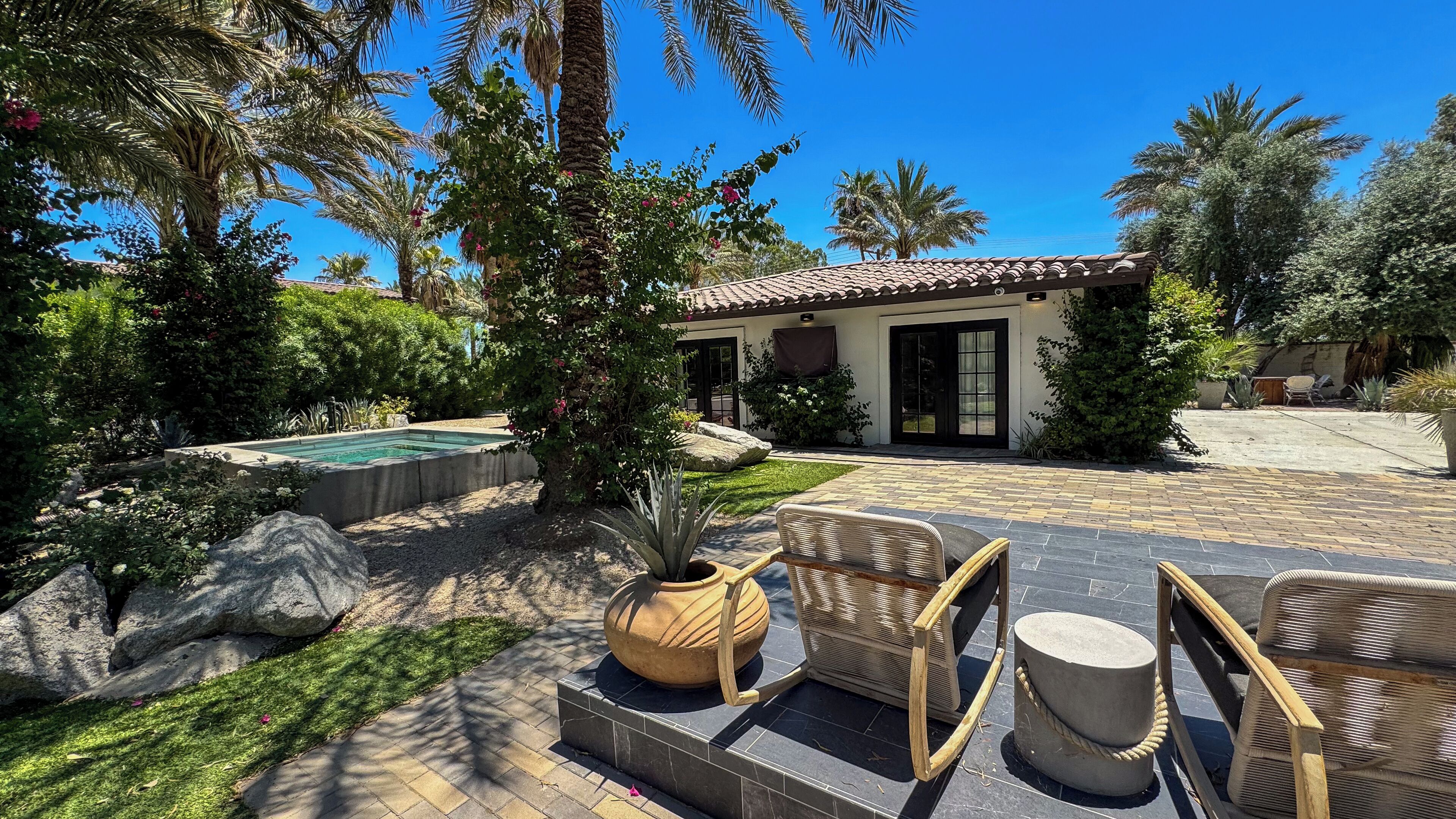 Un jardin avec une piscine, du mobilier d’extérieur et une maison avec un toit en tuiles.