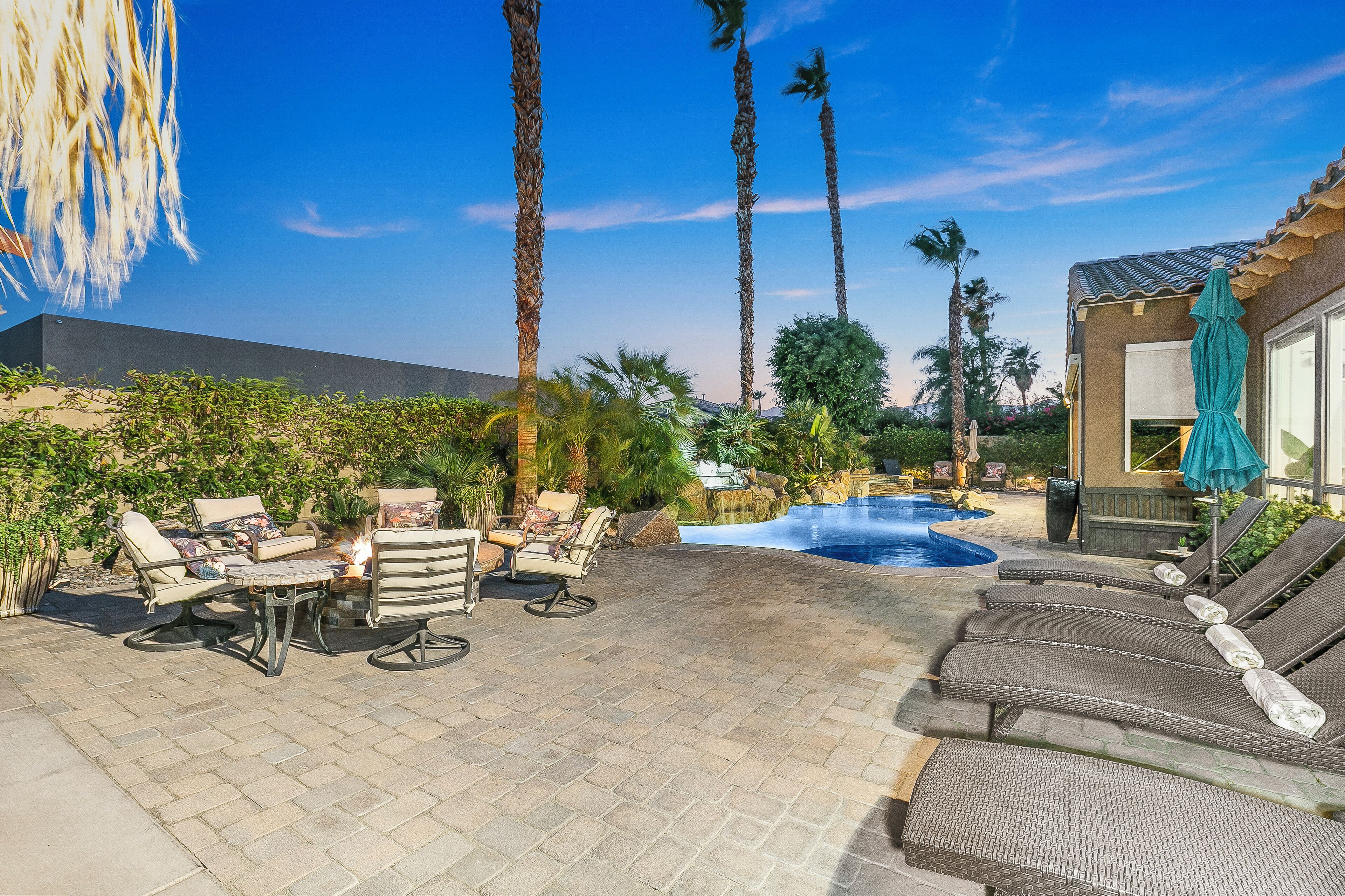 A patio with lounge chairs, a fire pit, and a swimming pool.